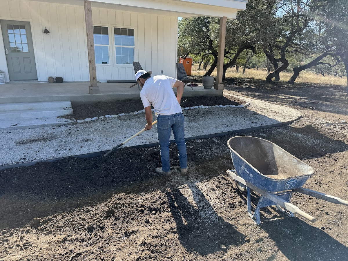 Isai Robles mulching soil outside a white farmhouse